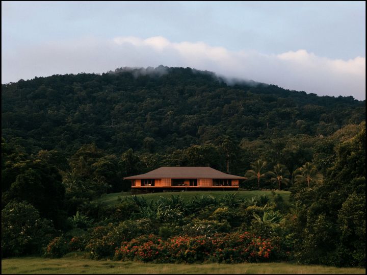 A hip roof with deep eaves over a raised timber house, the hill falling away behind