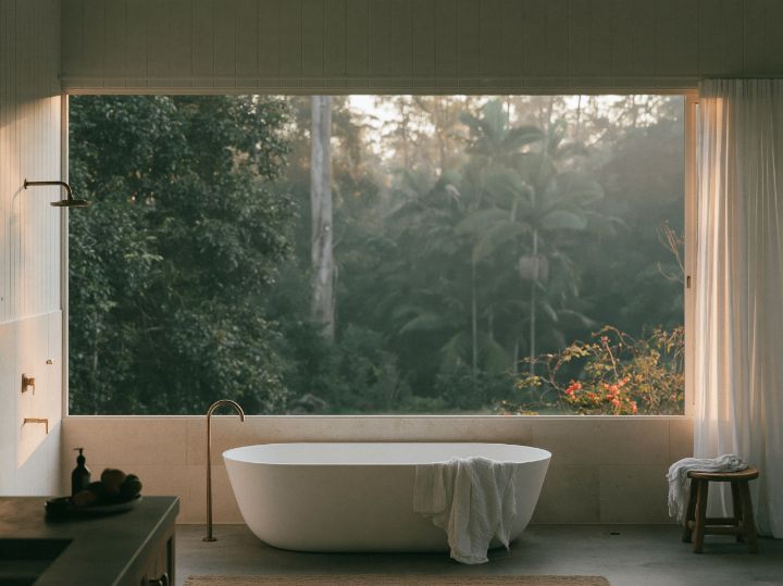 A pale stone bathroom with a freestanding bath and a window onto the garden