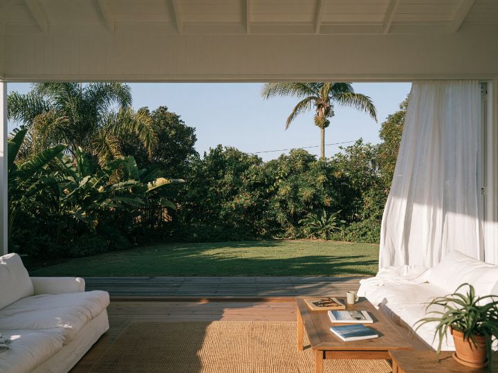 A living room open on two sides, linen and pale timber, the sea breeze coming through