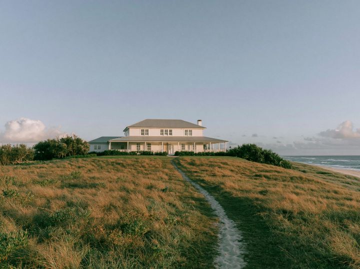 White weatherboards under a broad gable, a deep verandah across the front, the dunes behind