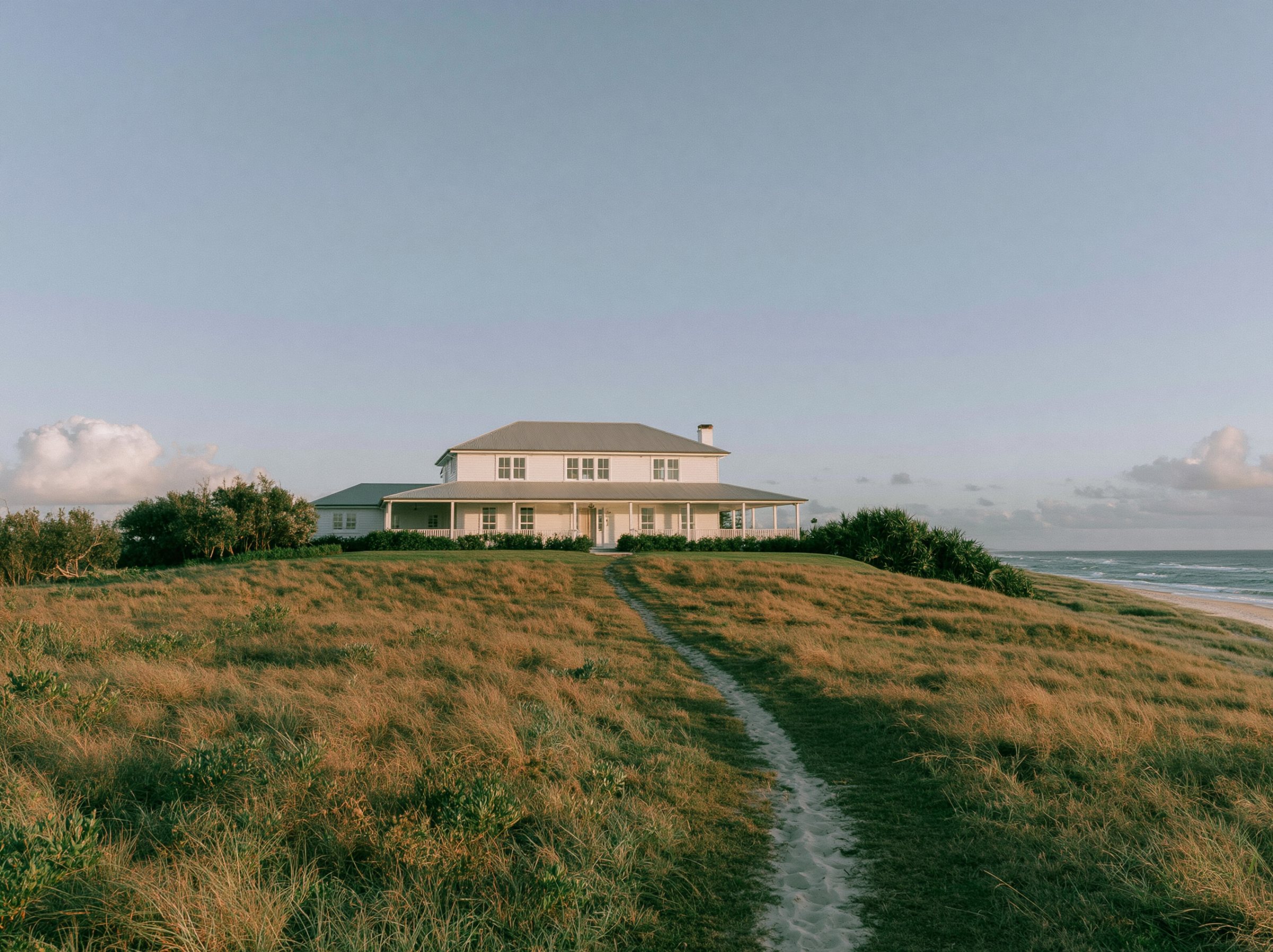 White weatherboards under a broad gable, a deep verandah across the front, the dunes behind