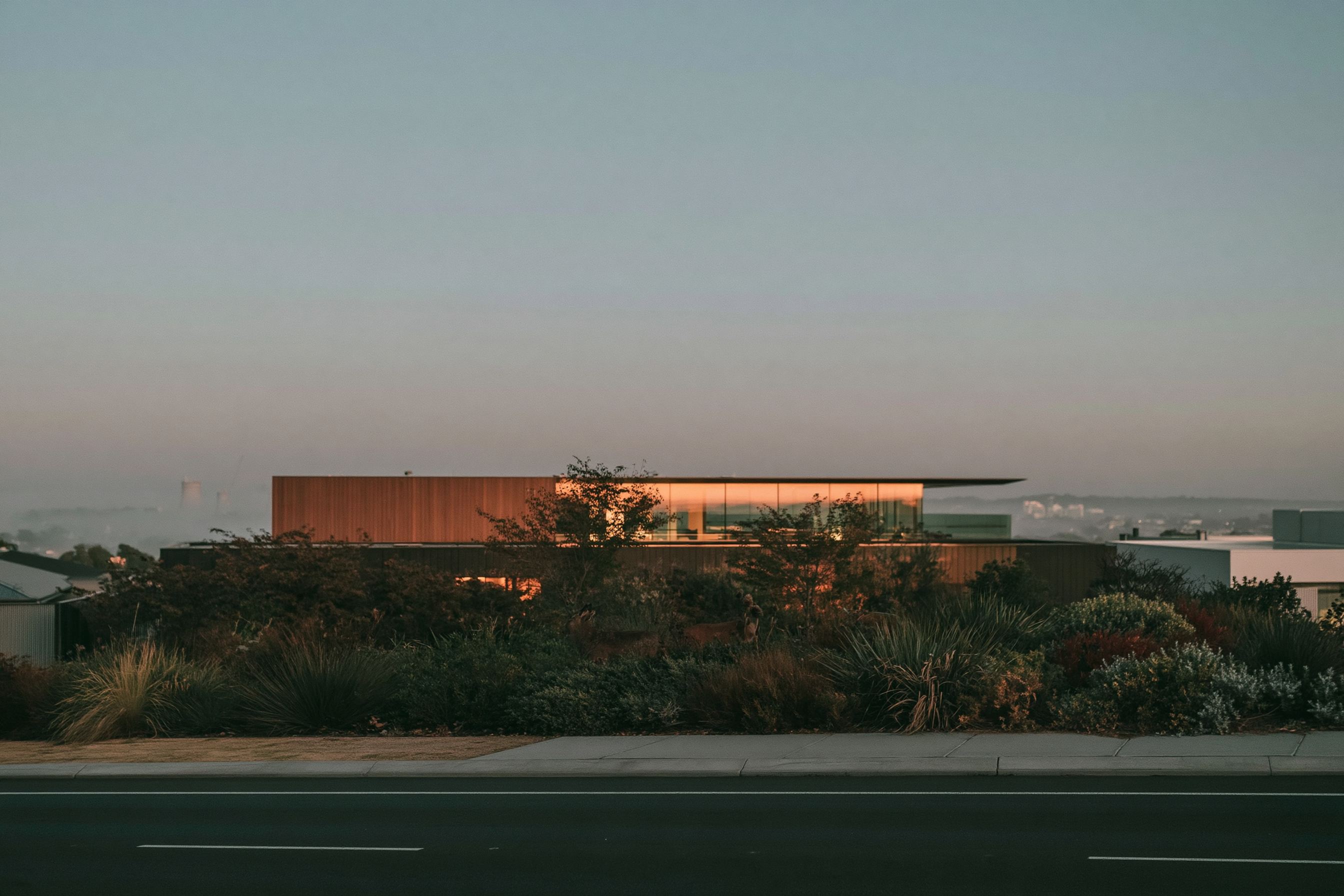 A long, low house at dusk with its lights on, seen from the road.